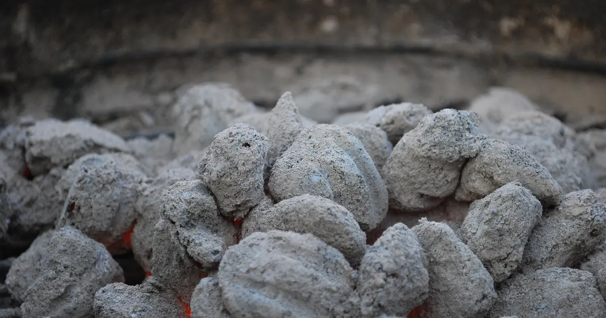 Charcoal briquettes covered in light grey ash on a grill, an example of charcoal ash color after burning